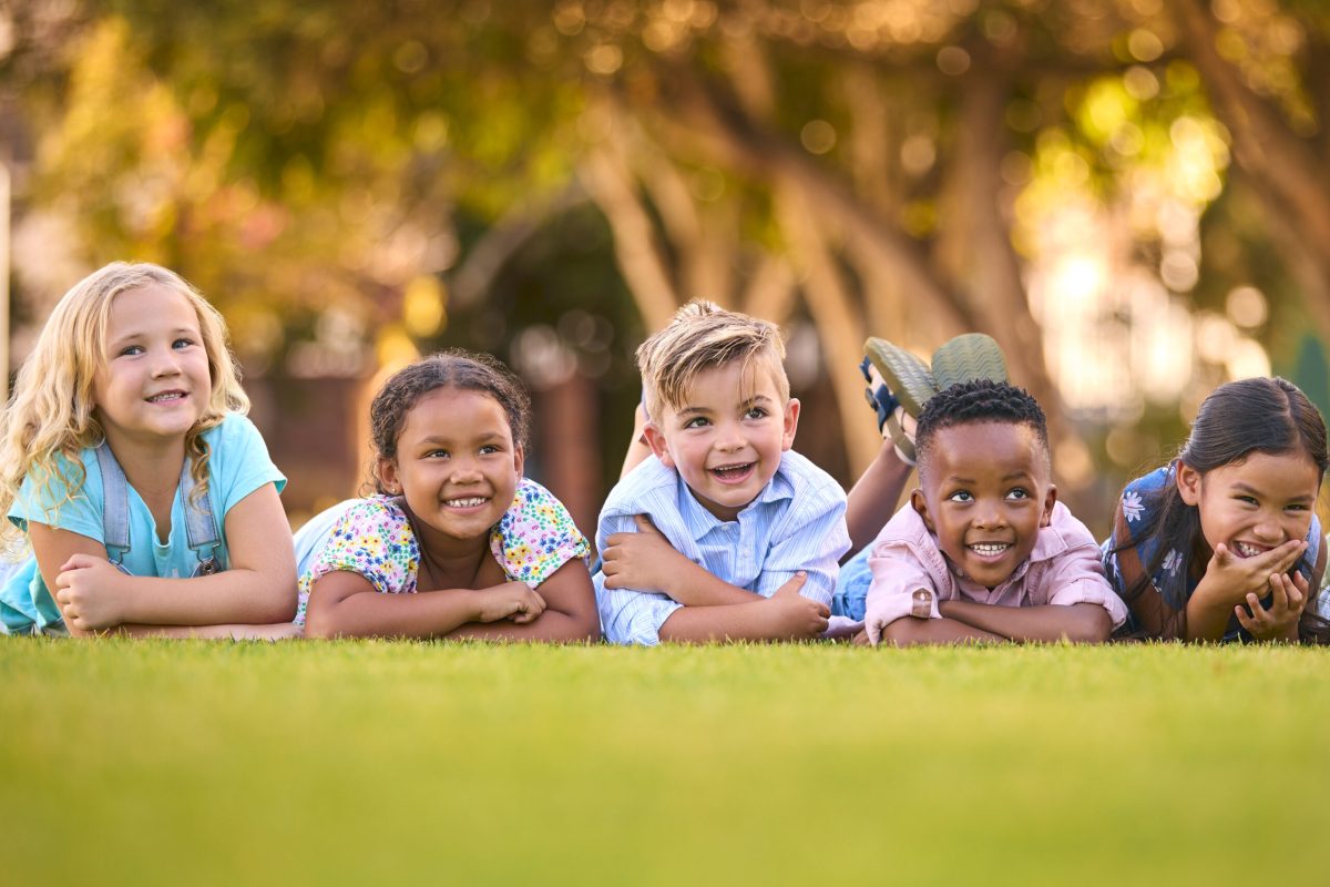 Portrait Of Multi-Cultural Primary Or Elementary School Student Friends Lying On Grass Outdoors